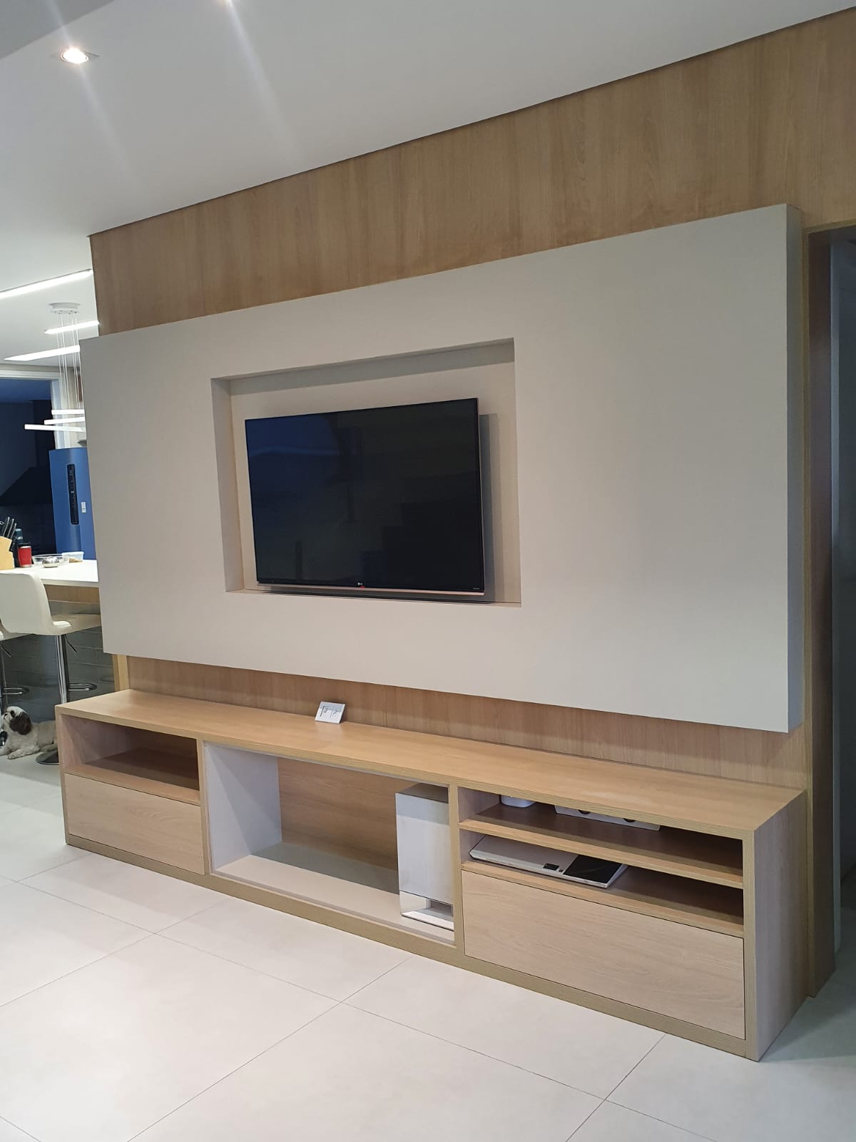 Painel grande para TV com nicho emoldurado e rack com gavetas e nichos abertos em sala integrada